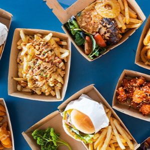 Blue background with cardboard food trays placed randomly all filled with food to takeaway